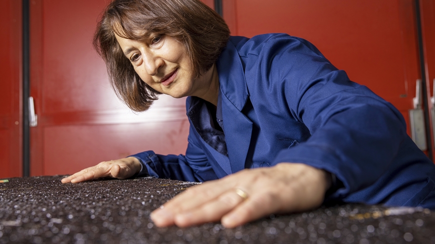 A photo of a woman with brown hair in a blue suit touching a stretch of recycled asphalt.