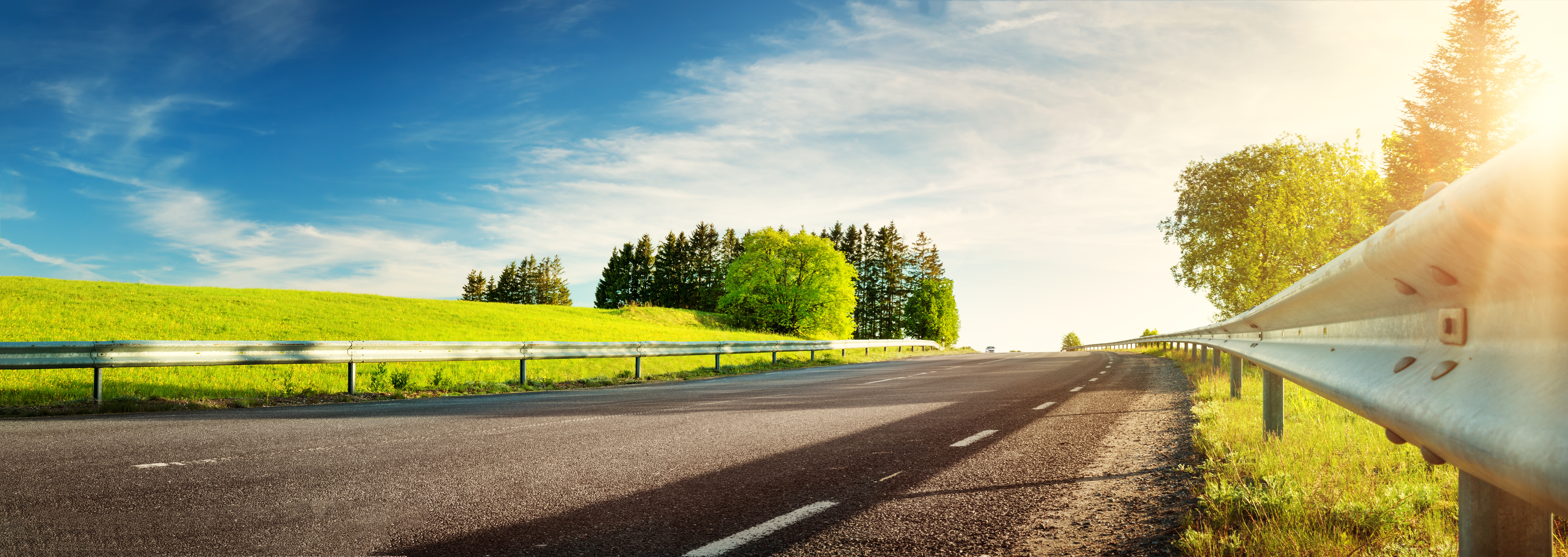 A photo of trees and green fields behind a highway.