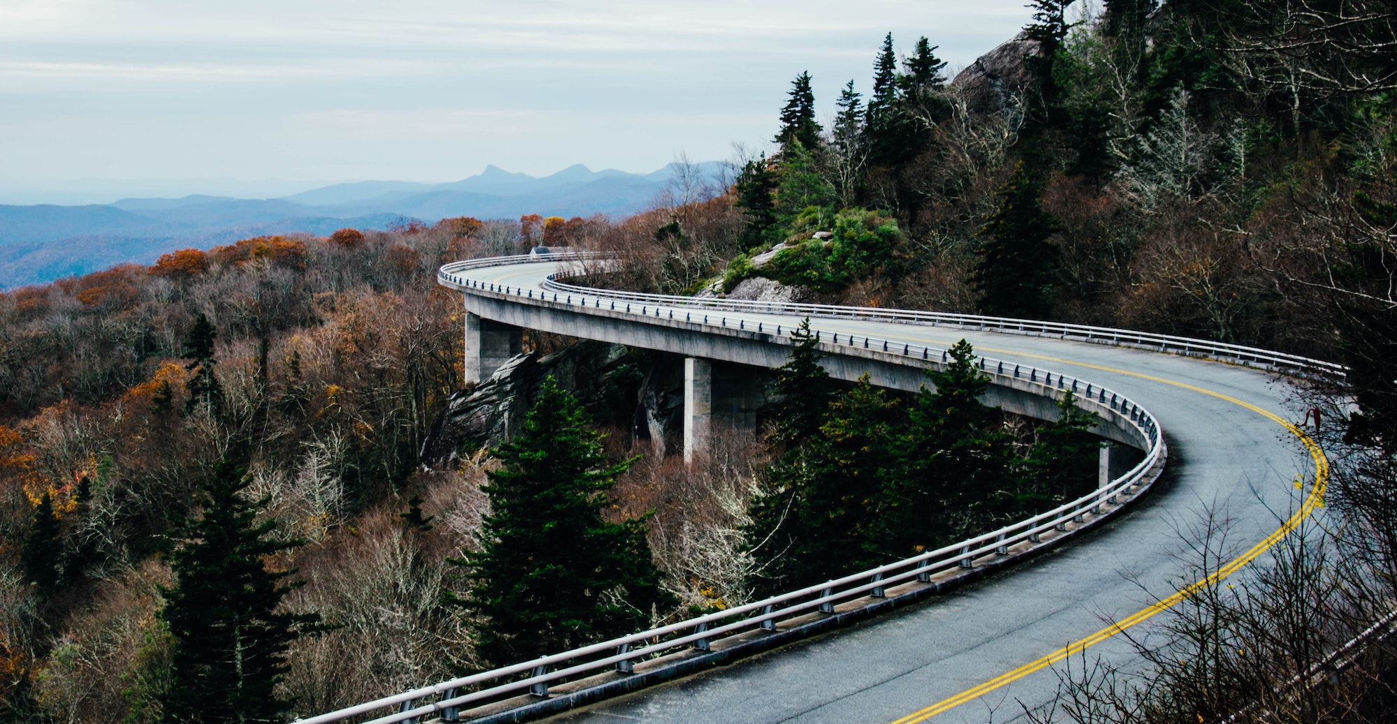 A picture of a road overpass twisting around the side of a forested mountain.